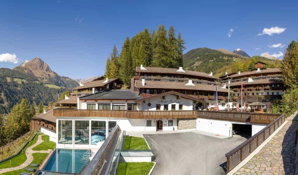 Hotel Goldried building with outdoor pool set against forested mountains under a clear blue sky.