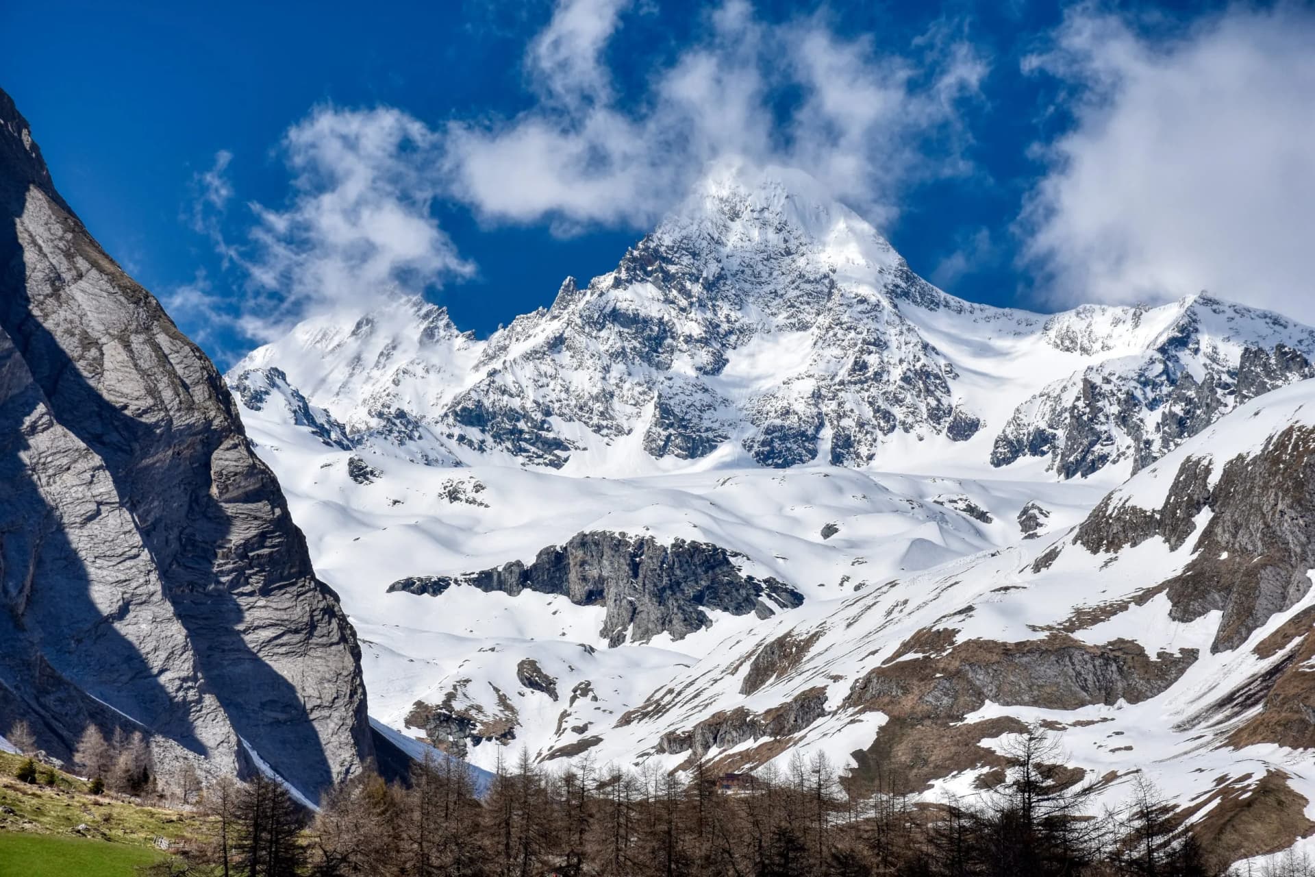 Snow-covered Grossglockner mountain peaks under a bright blue sky with white clouds in winter.