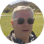 Man wearing sunglasses on a sunny golf course with arid mountains in the background.