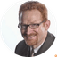 Close-up portrait of man with red hair and glasses smiling against white background