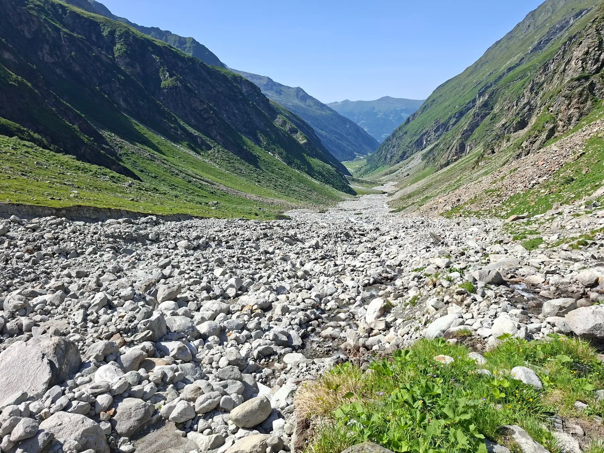 Rocky mountain valley with green slopes and a clear blue sky in the Hohe Tauern.