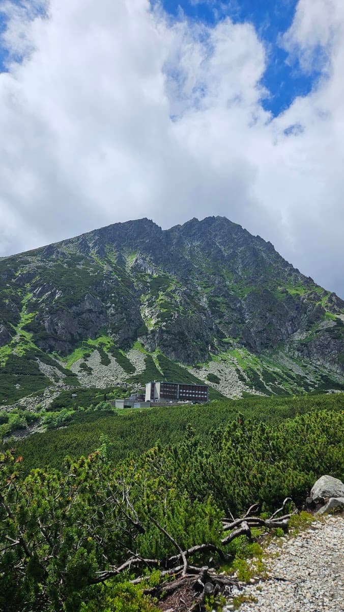 Alpine mountain peak with rocky slopes and a building at the base under a cloudy sky