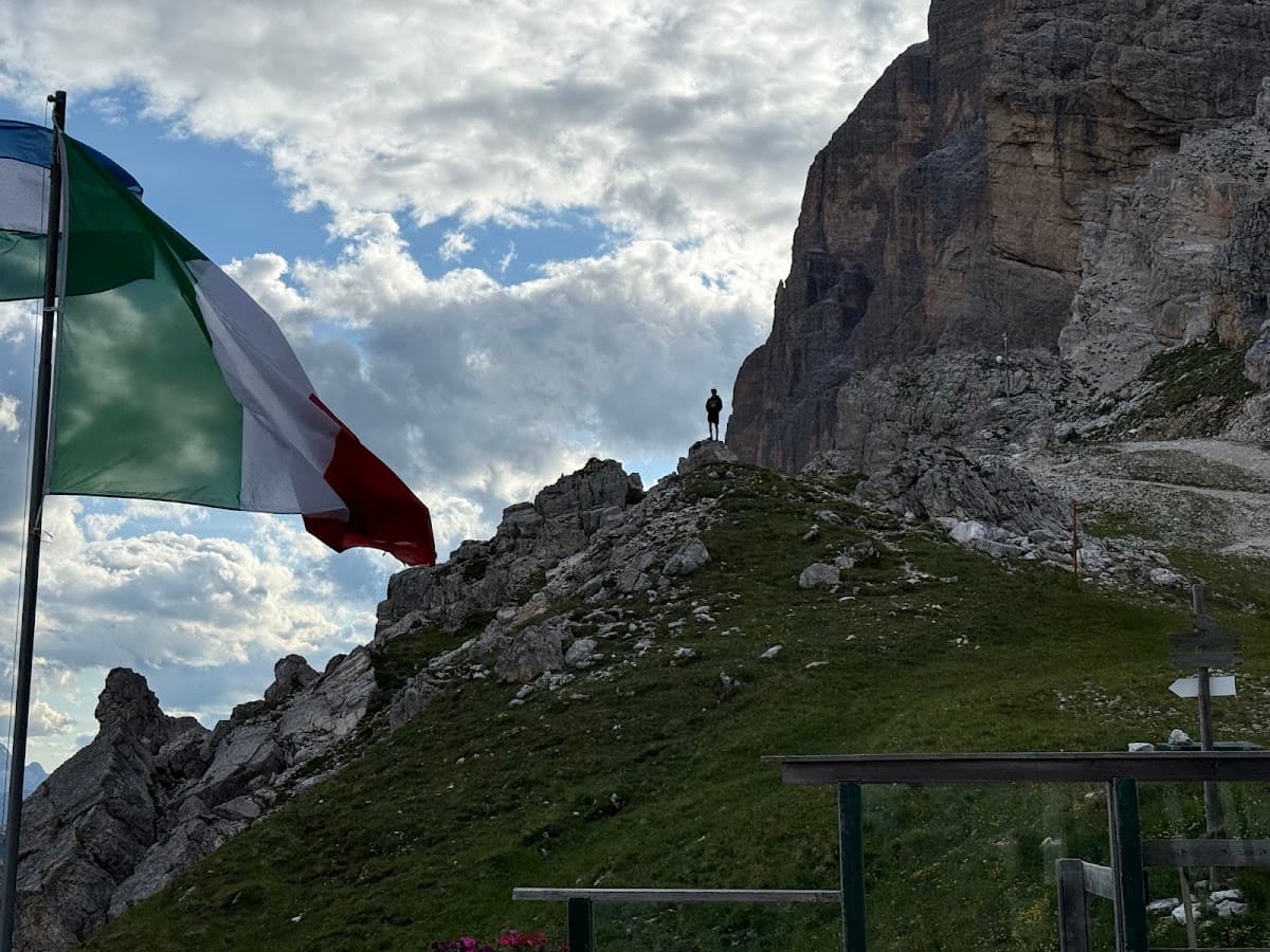 Hiker standing on rocky mountain ridge with Italian flag and cliffs