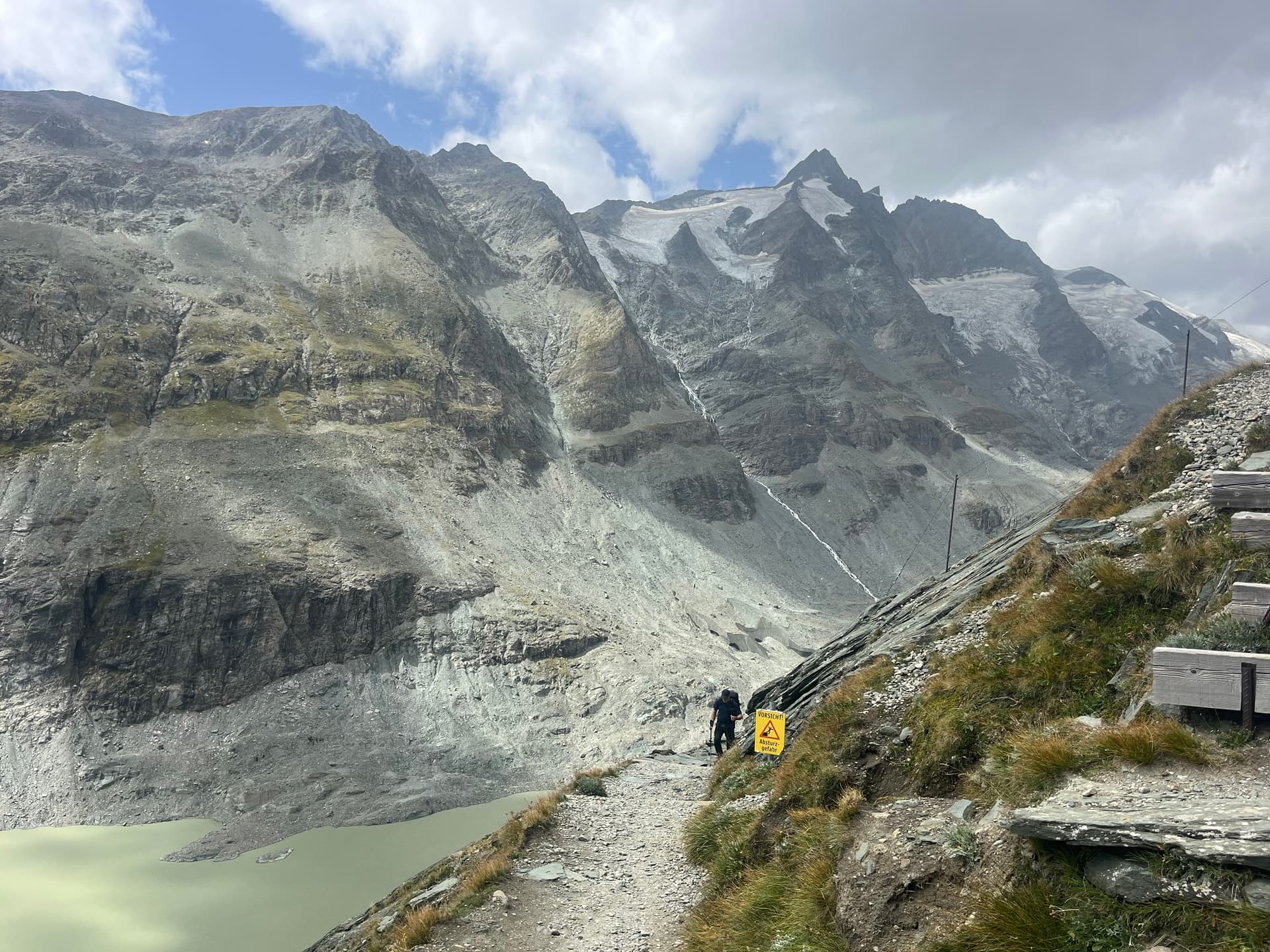 Hiker on a mountain path above a glacier lake with rocky peaks
