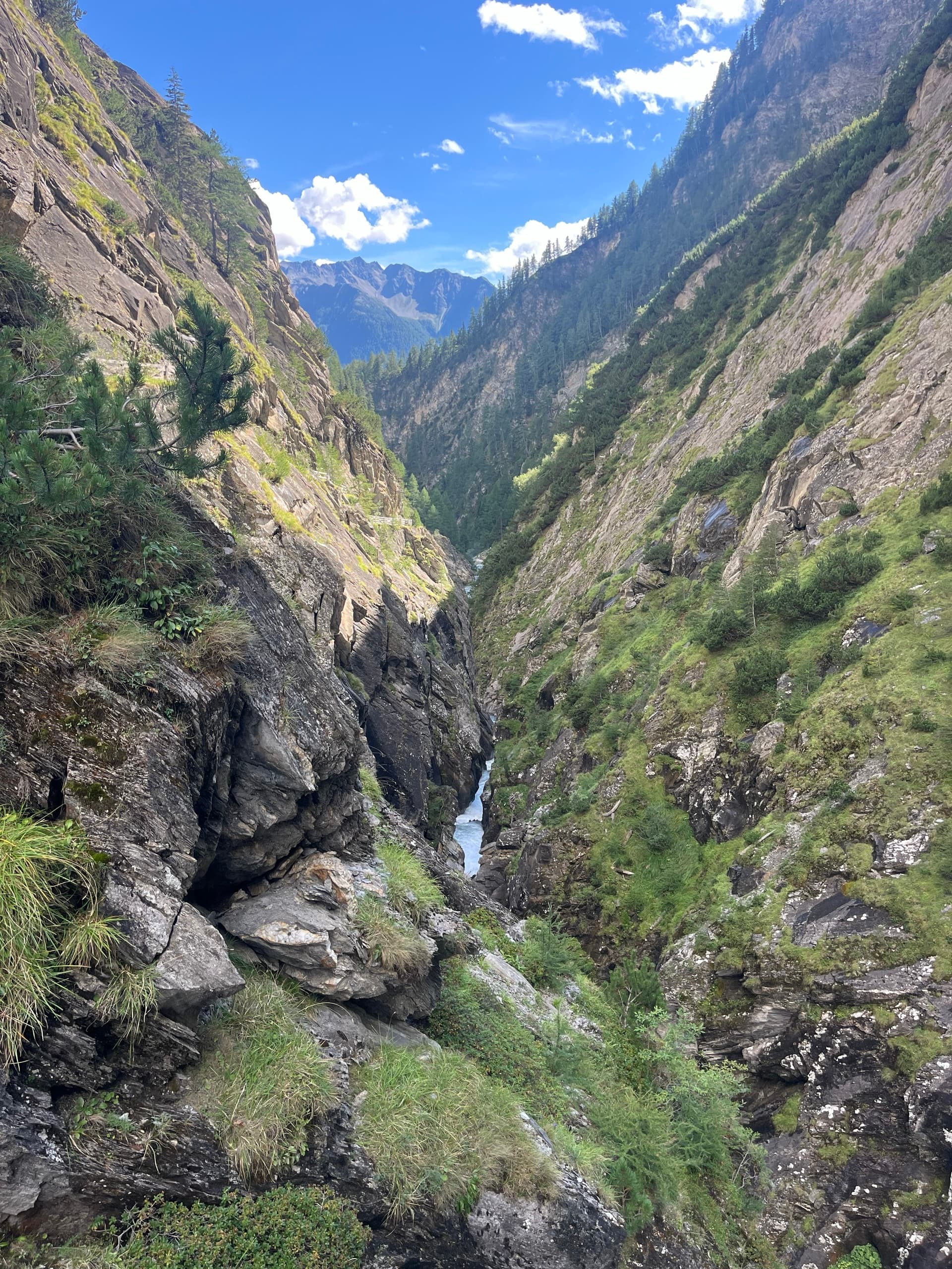 Deep mountain gorge with steep rocky cliffs and a white stream below