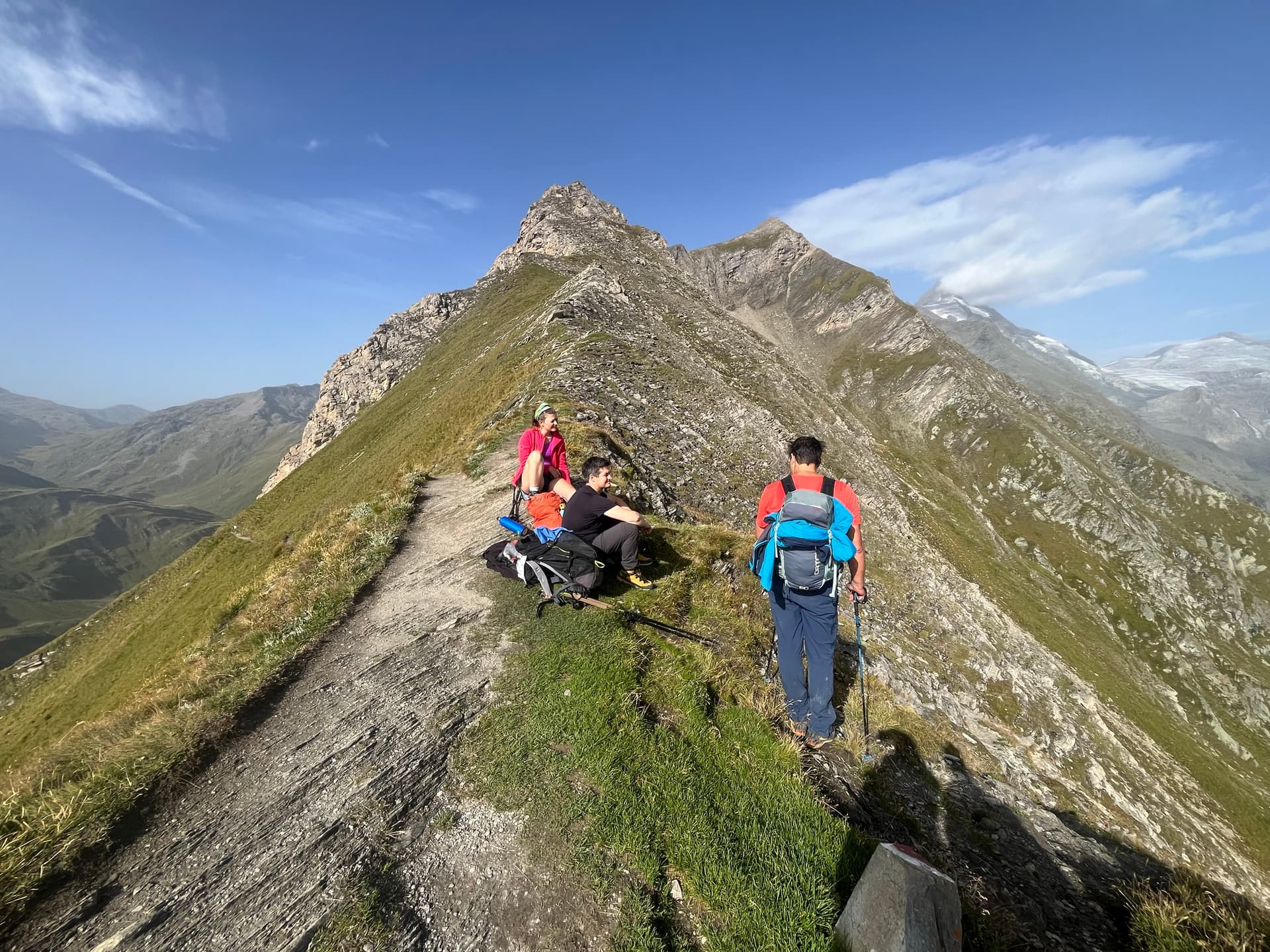 Hikers resting on a grassy ridge in alpine mountains