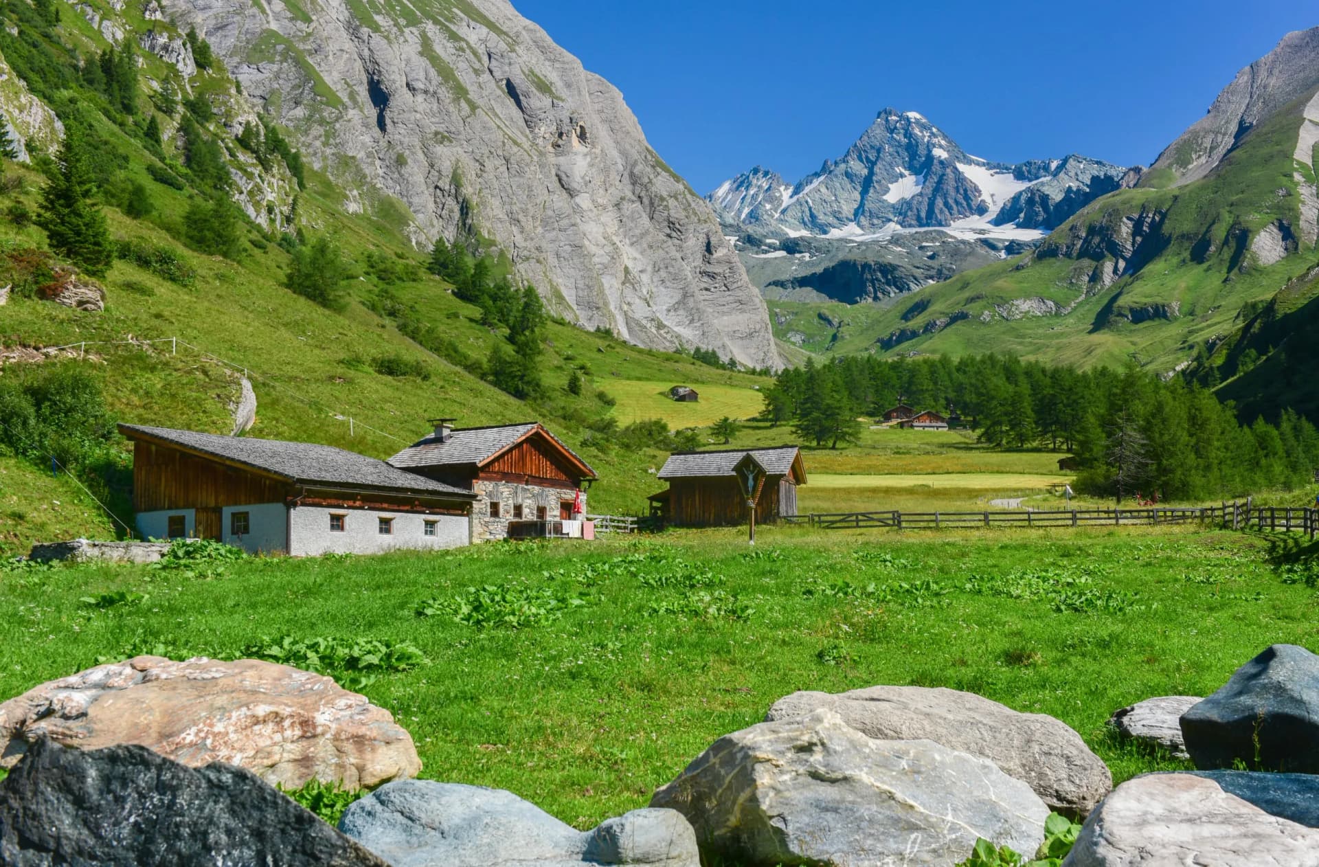 Alpine meadow with stone huts, green slopes, and snow-capped Grossglockner mountain.