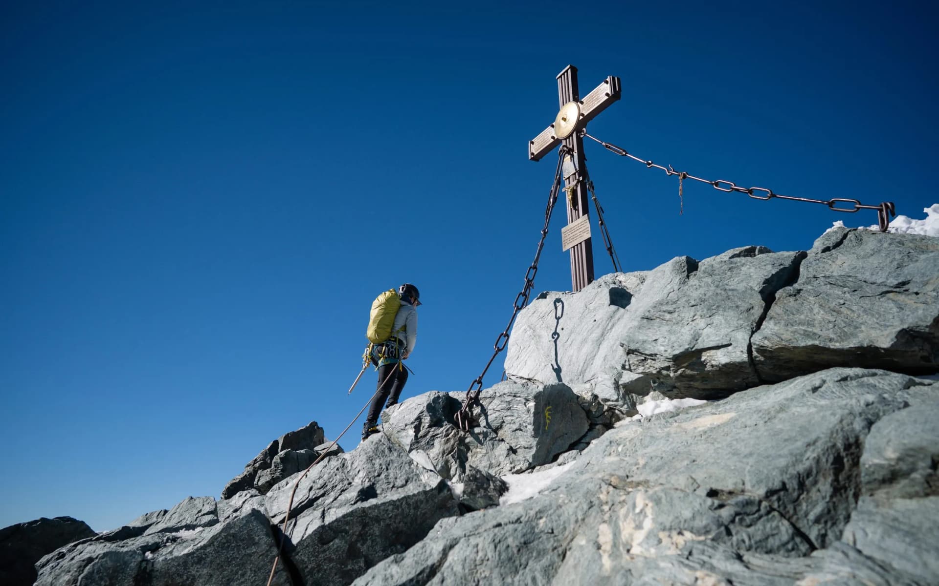Hiker reaching summit cross on Grossglockner mountain rocks under clear blue sky