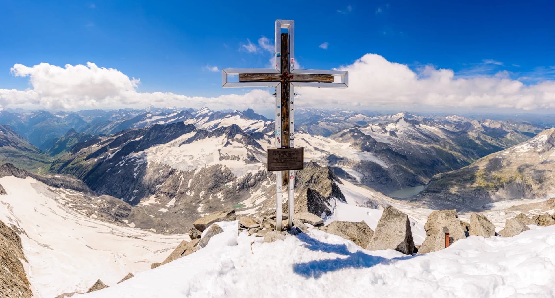 Summit cross on snowy Grossvenediger mountain peak overlooking glaciers and alpine ranges