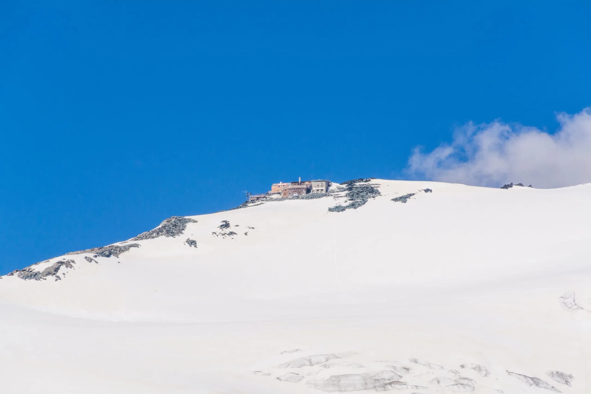 Erzherzog Johann Hütte mountain hut perched on a snow-covered alpine peak under a bright blue sky.